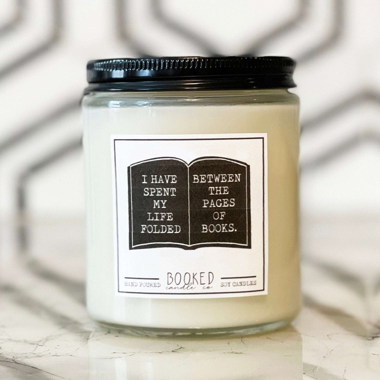 Image of a handmade candle in a glass container with a book label saying "I Have Spent My Life Folded Between The Pages Of Books"