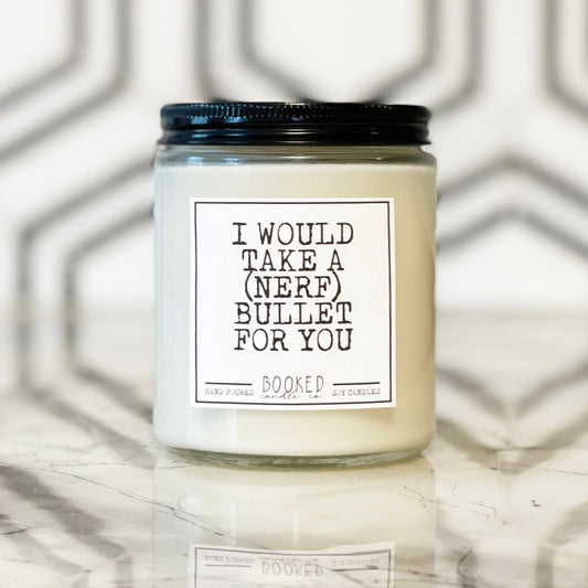 Image of a handmade candle in a glass container with a book label saying "I Would Take A (Nerf) Bullet For You"