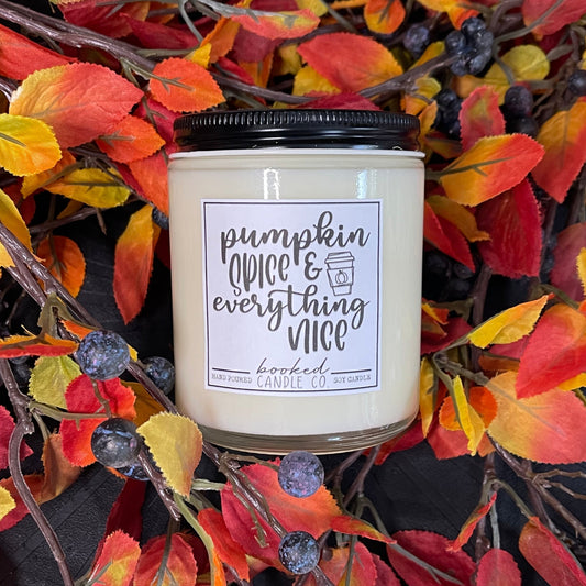 Candle with 'pumpkin spice & everything nice' label on autumn leaves