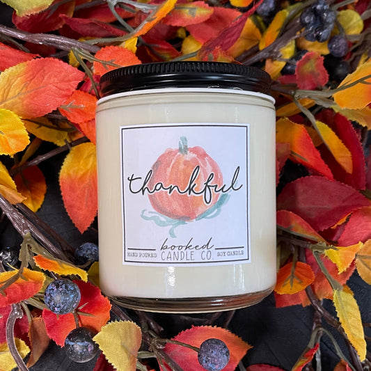 Candle with a 'thankful' label surrounded by autumn leaves and berries