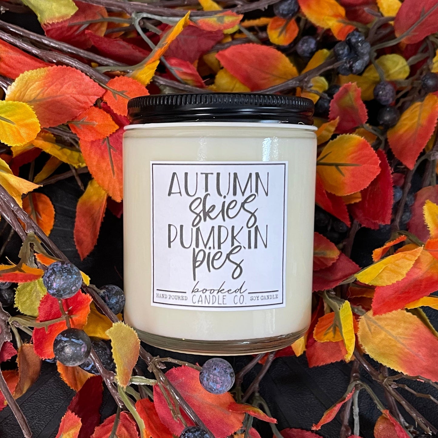 Candle with 'Autumn Skies Pumpkin Pies' label on a decorative wreath with fall leaves and berries