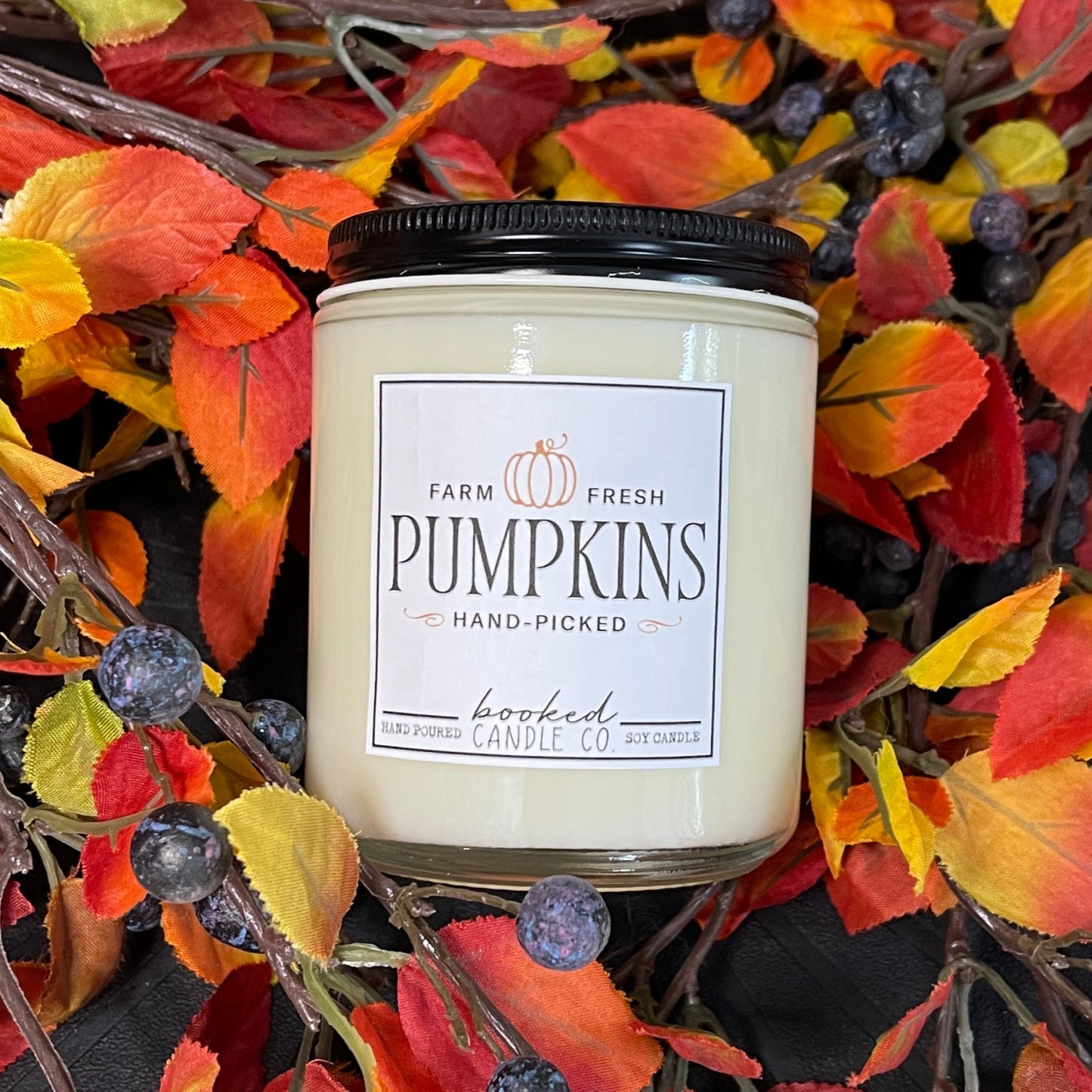 Candle with a 'Farm Fresh Pumpkins' label surrounded by autumn leaves and berries