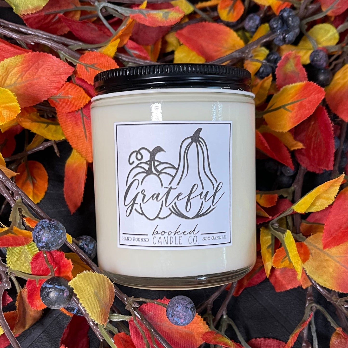 Candle with 'Grateful' label surrounded by autumn leaves and berries