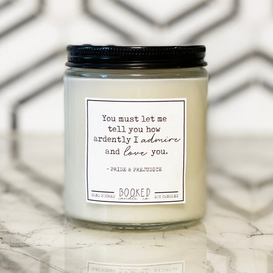 A white soy wax candle in an 8oz glass jar with a black lid, labeled 'Ardently Admire And Love - Pride & Prejudice' on a marble surface.