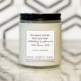 A white soy wax candle in an 8oz glass jar with a black lid, labeled 'Ardently Admire And Love - Pride & Prejudice' on a marble surface.