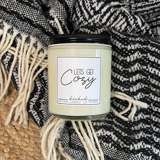 Candle with 'Let's Get Cozy' label on a textured blanket